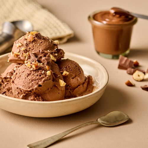 Schokoladeneis mit gehackten Nüssen in einer Schale, daneben ein Glas Schokoladencreme, Löffel und Nüsse.