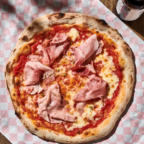 Pizza mit Tomatensoße, Käse und Schinken auf karierter Unterlage.