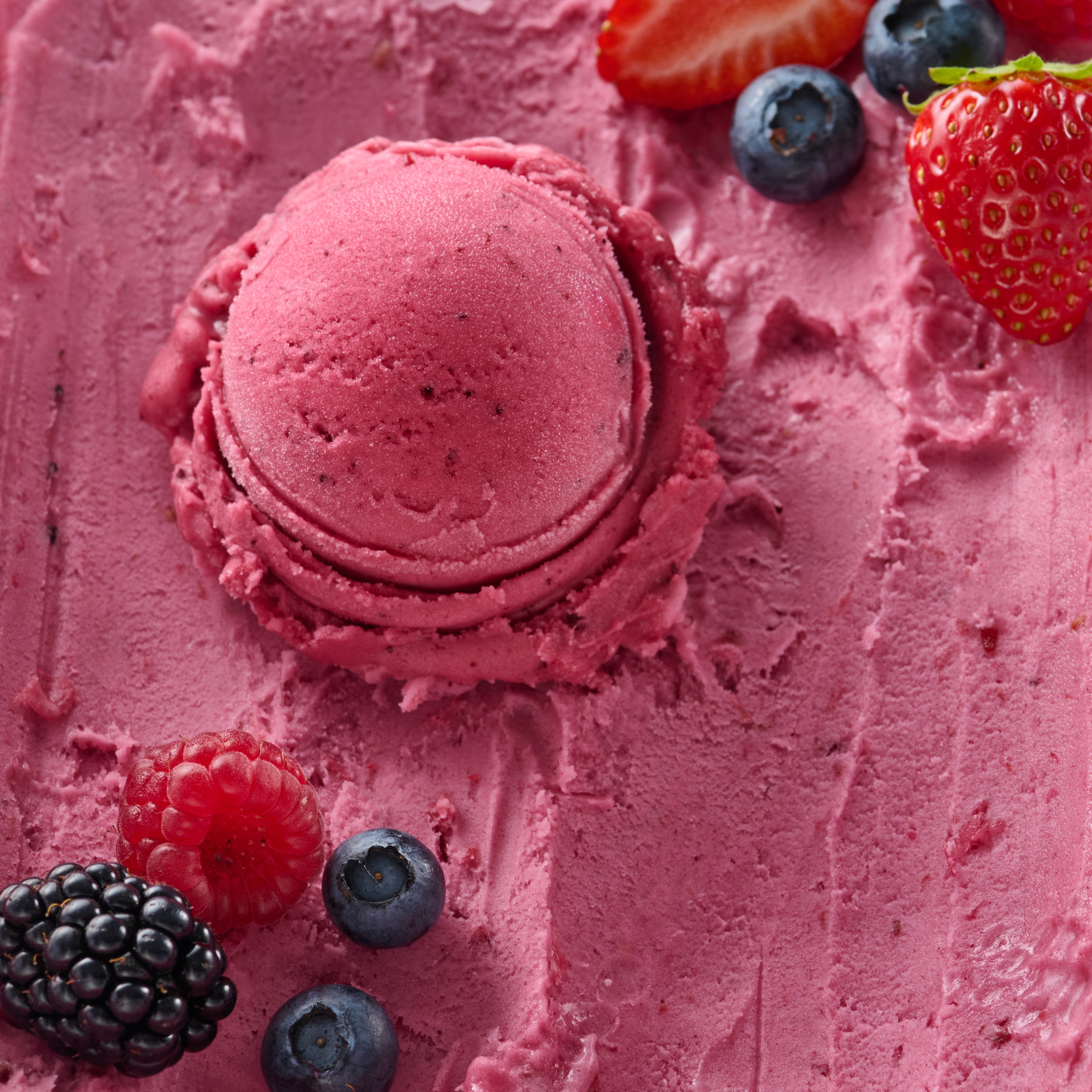 Eine Kugel pinkfarbenes Eis mit Erdbeeren, Blaubeeren, Himbeeren und Brombeeren auf glatter Eisoberfläche.
