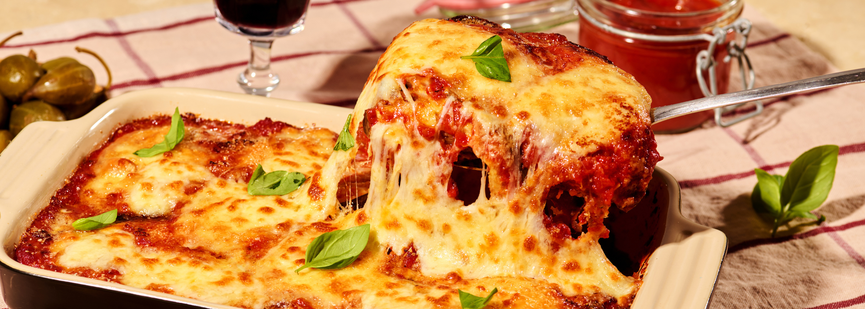 Überbackene Lasagne mit geschmolzenem Käse und Basilikumblättern, serviert in einer Auflaufform auf kariertem Tuch.