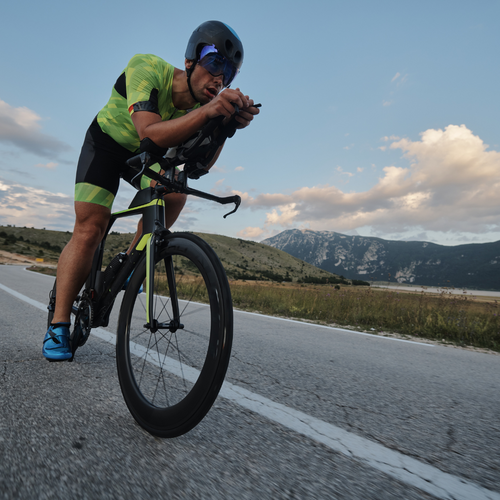 Ein Radfahrer mit Helm und Sonnenbrille fährt auf einer Landstraße vor einer Berglandschaft.