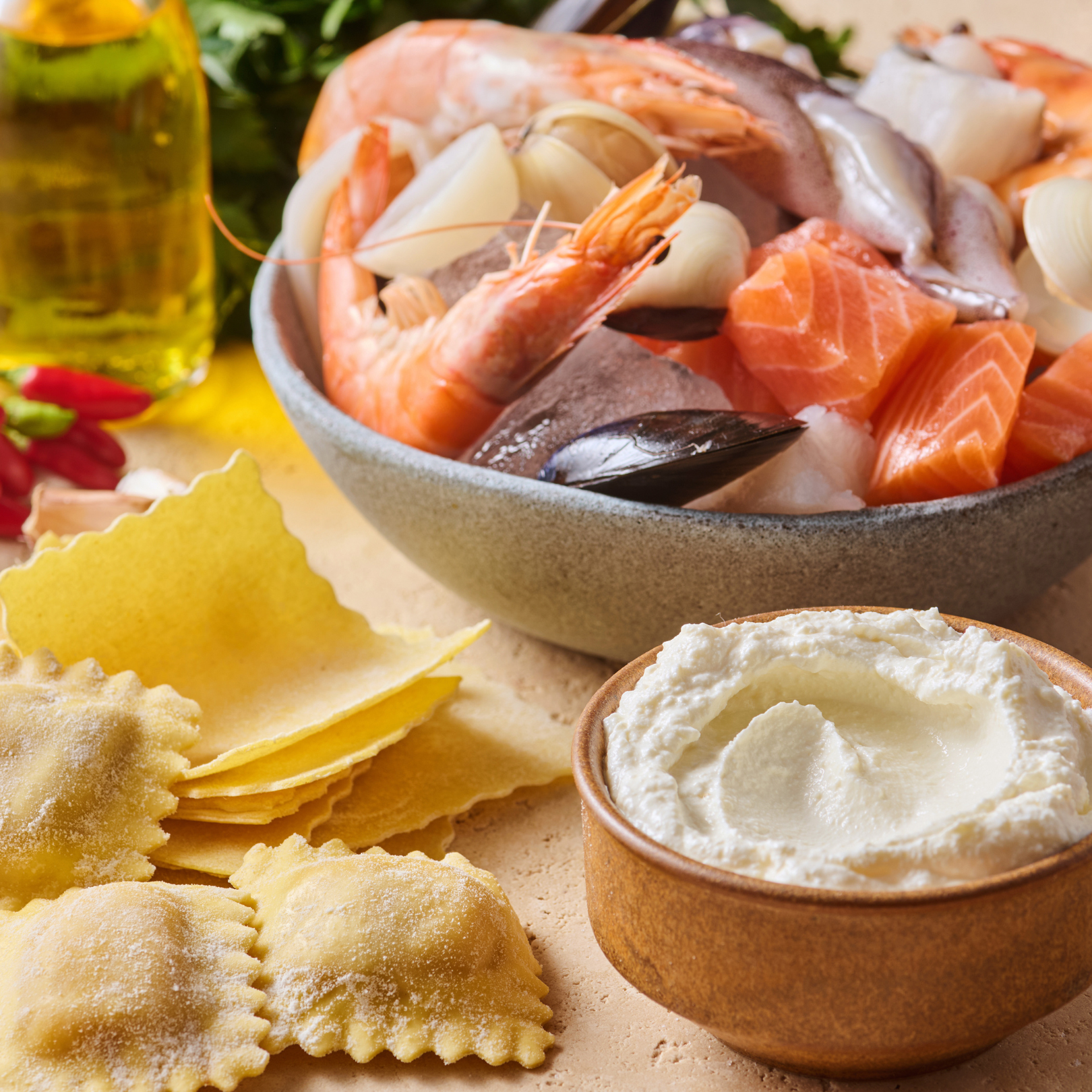 Schale mit frischem Meeresfrüchten neben Ravioli-Teig und einer Schüssel mit Frischkäse auf einem Tisch.
