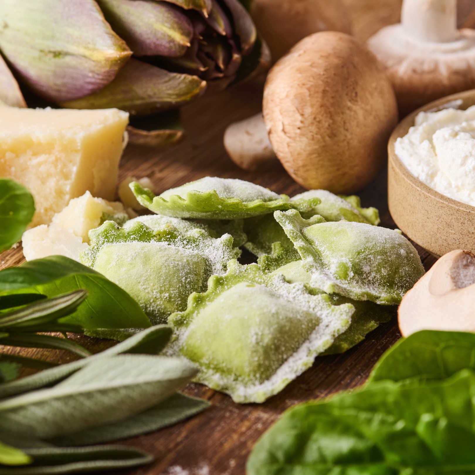 Grüne Ravioli auf einem Holzbrett mit Parmesan, Artischocken, Pilzen, Ricotta und frischem Spinat.