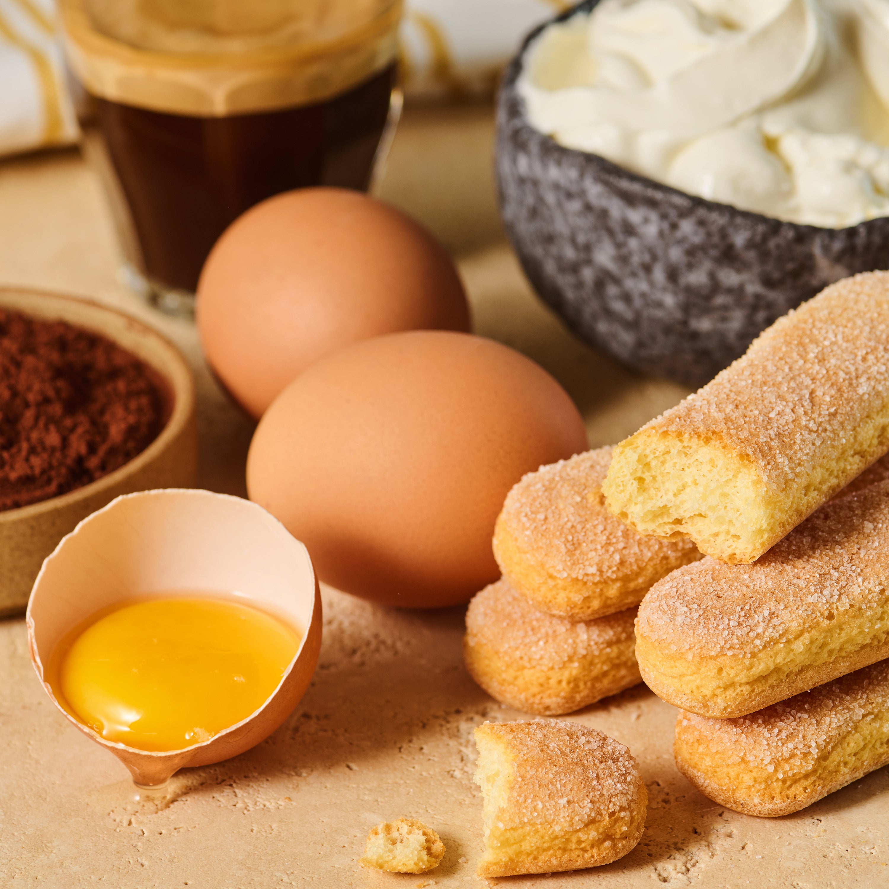 Eier, Löffelbiskuits, Kakaopulver und geschlagene Sahne auf einer Tischplatte, perfekt für ein Dessert.