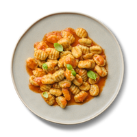 Ein Teller Gnocchi mit Tomatensauce und Basilikumblättern auf schwarzem Hintergrund.