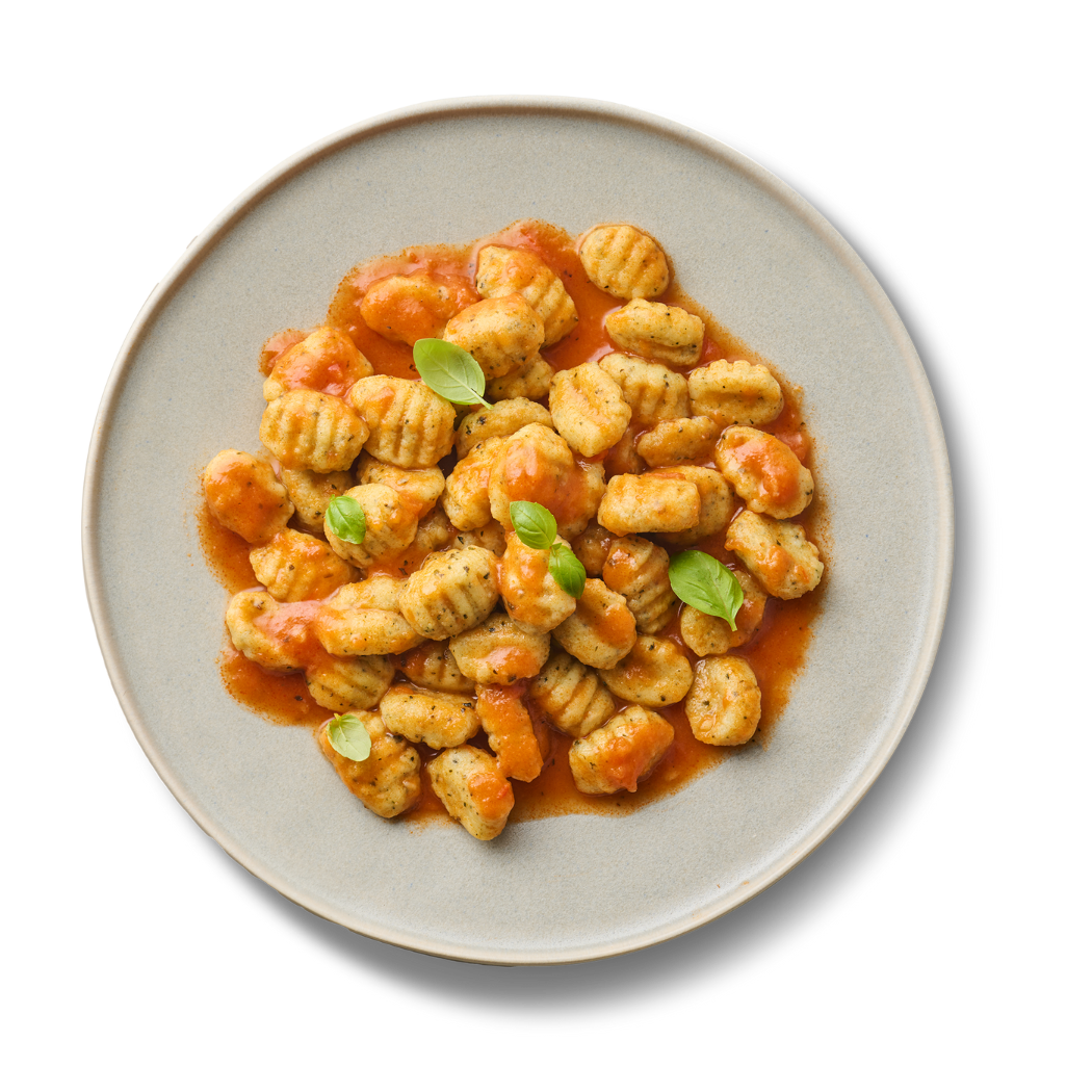 Ein Teller Gnocchi mit Tomatensoße und Basilikumblättern, aus der Vogelperspektive fotografiert.
