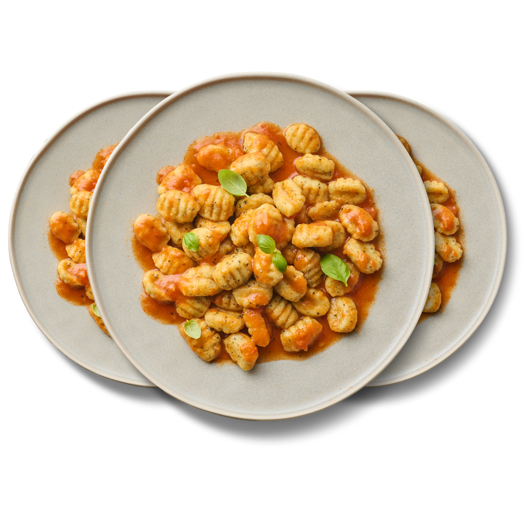 Drei Teller mit Gnocchi und Tomatensauce, garniert mit Basilikumblättern.