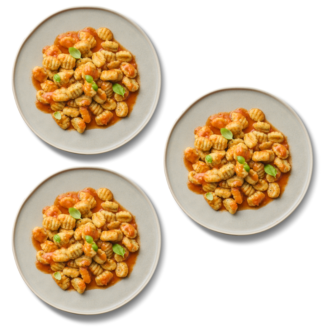 Drei Teller mit Gnocchi in Tomatensauce, garniert mit frischen Basilikumblättern.