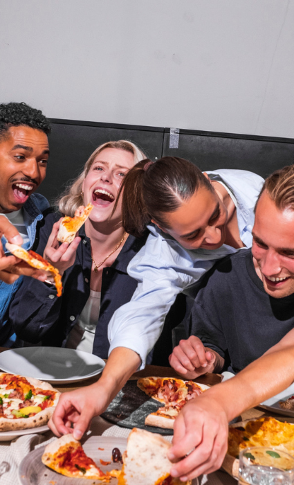 Vier lachende Menschen teilen Pizza in geselliger Runde.
