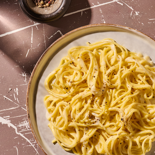 Ein Teller mit cremiger Pasta, garniert mit Pfeffer, daneben eine Schale bunter Pfefferkörner.