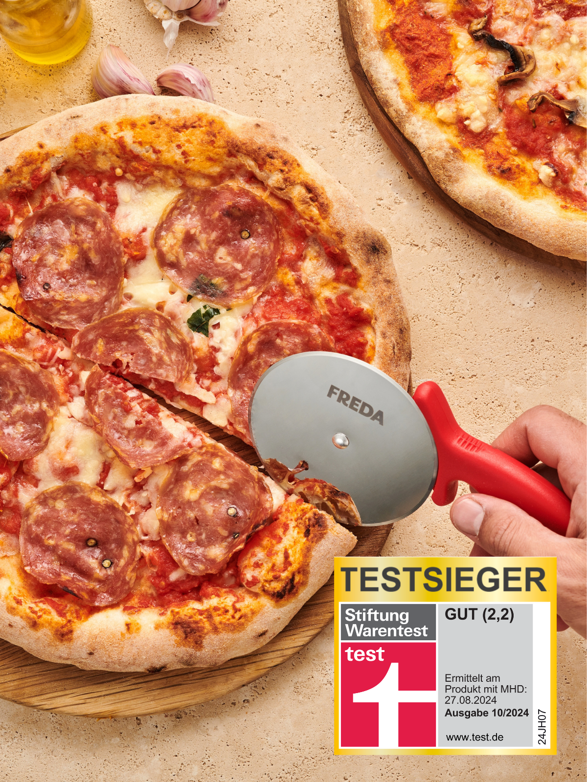 Nahaufnahme einer Person, die mit einem Pizzaschneider eine Salami-Pizza schneidet, daneben ein Testurteilssiegel.