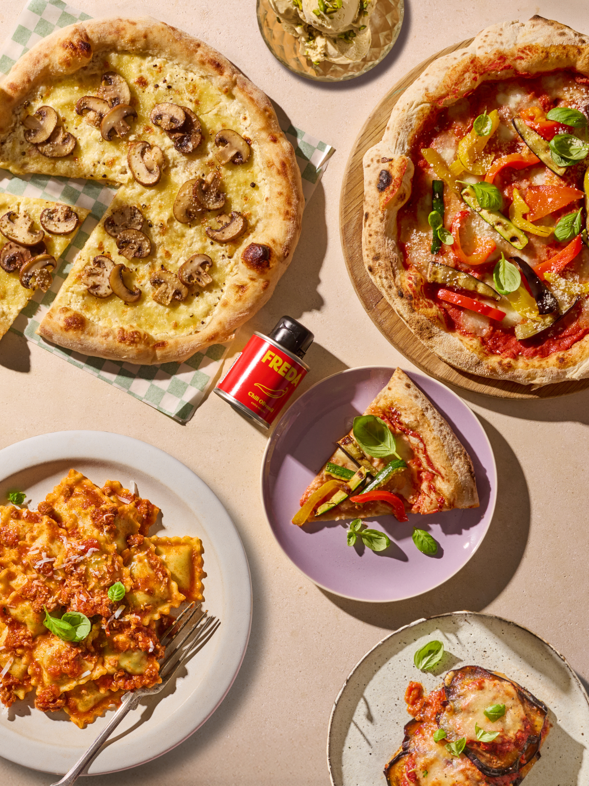 Verschiedene italienische Gerichte, darunter Pizzen mit Pilzen und Gemüse, Ravioli und gebackene Auberginen, auf einem Tisch.