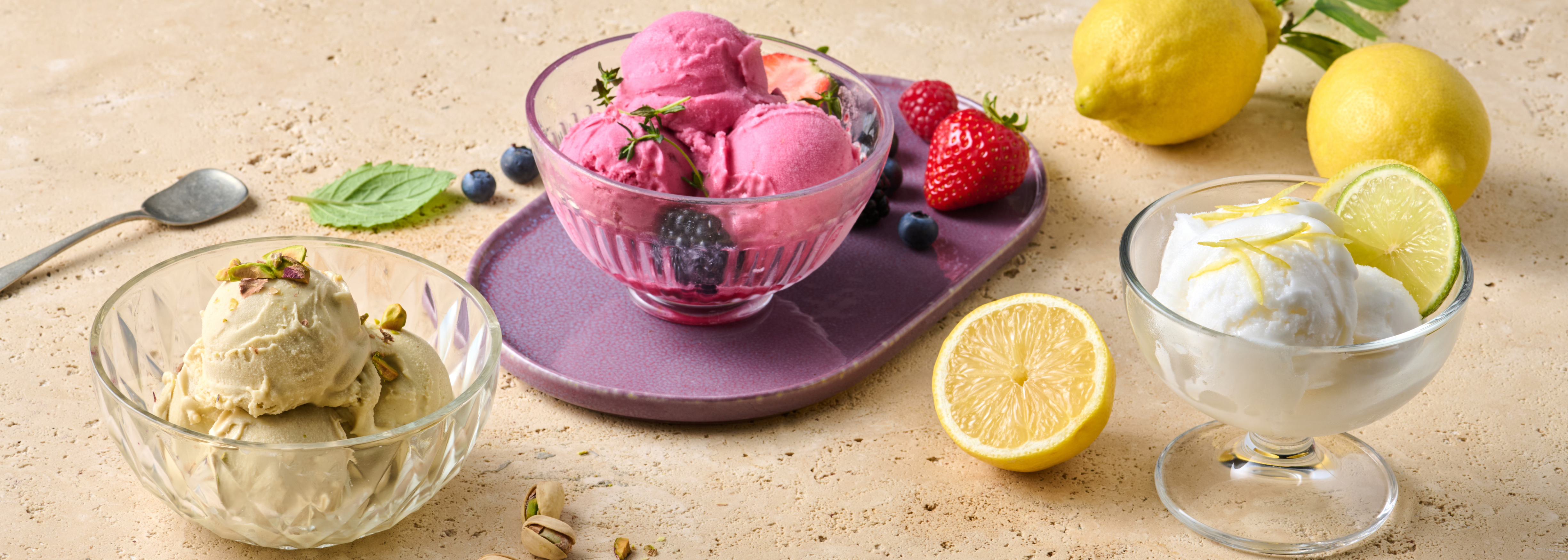 Drei Schalen Eiscreme mit verschiedenen Geschmacksrichtungen, umgeben von Zitronen, Erdbeeren und Blaubeeren.