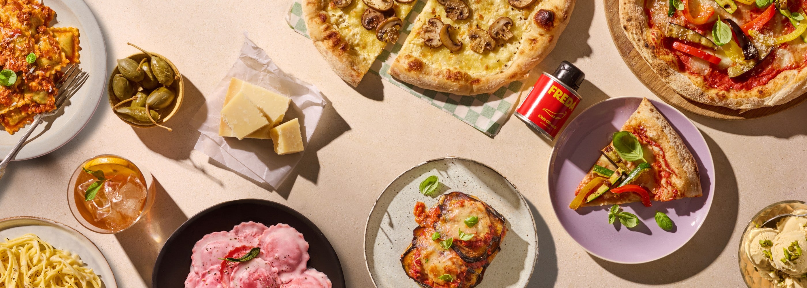 Verschiedene italienische Gerichte, darunter Pizza, Pasta, Käse und ein Getränk, auf einem Tisch arrangiert.