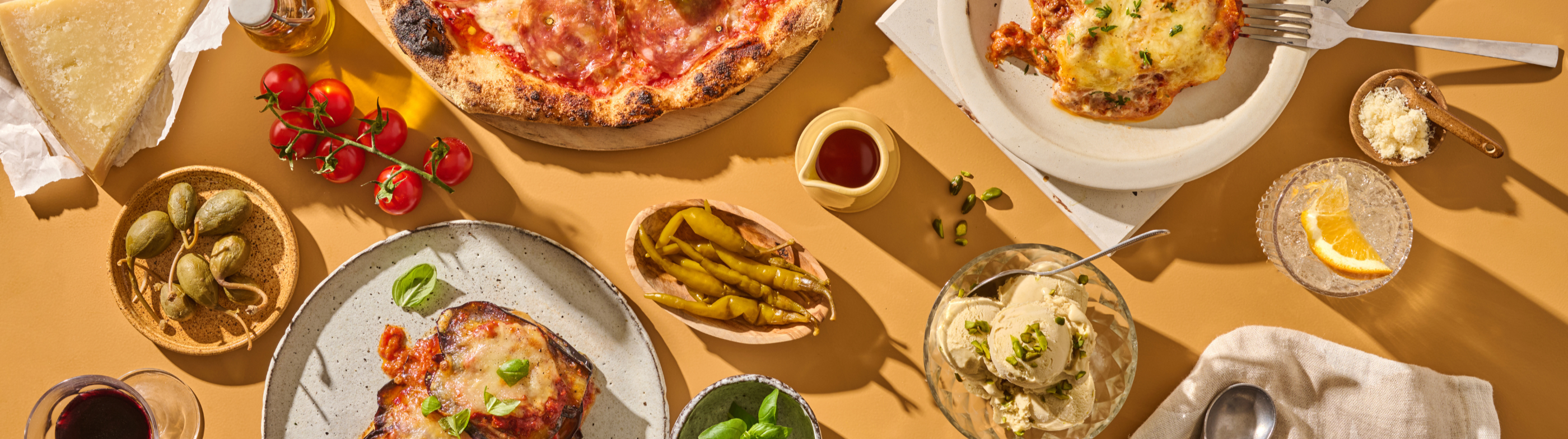 Verschiedene italienische Gerichte, darunter Pizza, Lasagne, Parmesan, Tomaten, und ein Getränk mit Orangenscheibe.