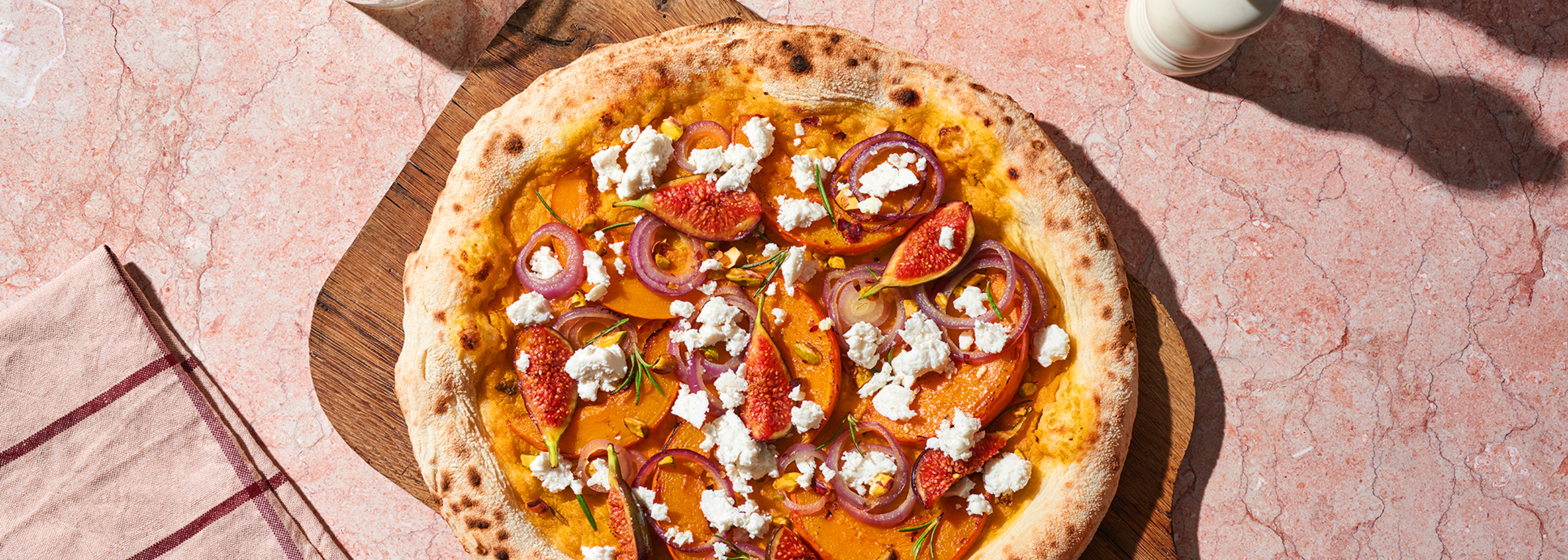 Pizza belegt mit Feigen, Kürbis, roten Zwiebeln und Feta auf einem runden Holzbrett.