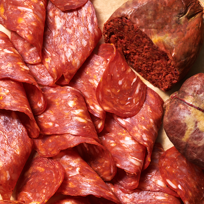 Aufgeschnittene rote Wurstscheiben neben einer teilweise aufgeschnittenen runden Wurst auf Papier.
