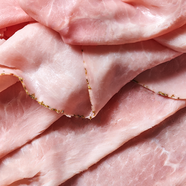 Nahaufnahme von dünn geschnittenem, rosa Schinken, übereinander gestapelt.