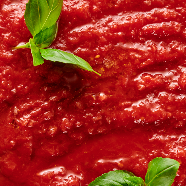 Nahaufnahme von Tomatensauce mit frischen Basilikumblättern.