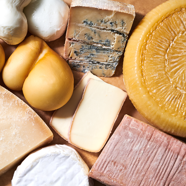 Verschiedene Käsesorten auf einem Holzbrett, darunter Blauschimmelkäse, Brie und Hartkäse.