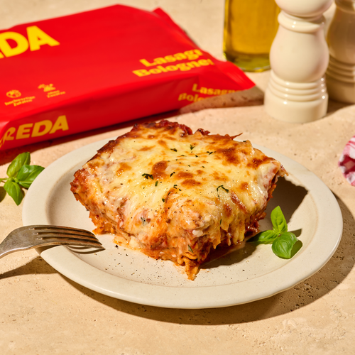 Ein Teller mit einem Stück Lasagne Bolognese, daneben eine Packung Lasagneblätter und eine Pfeffermühle.