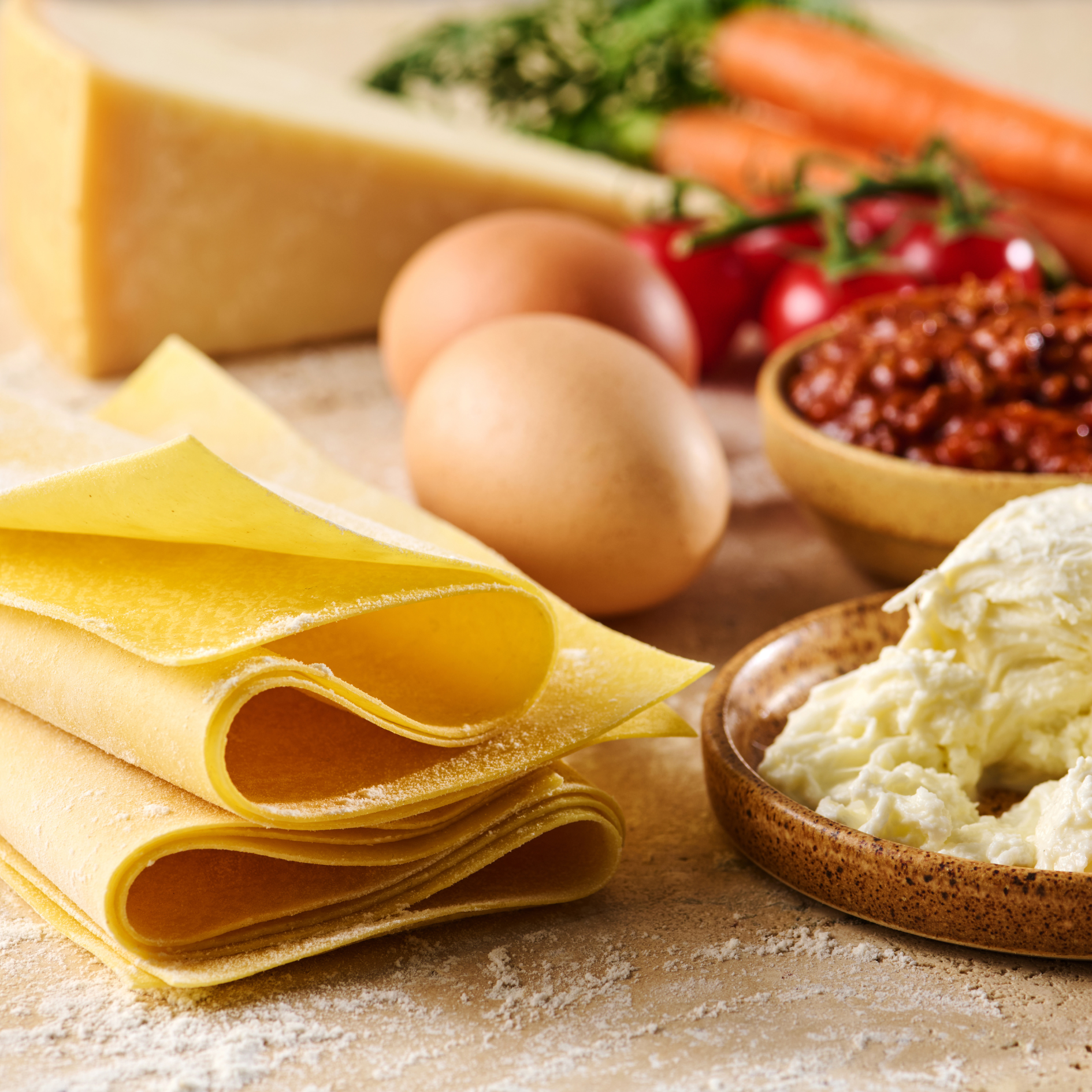 Verschiedene Lasagne-Zutaten, darunter frische Nudeln, Eier, Käse, Tomatensauce, Karotten und Tomaten.