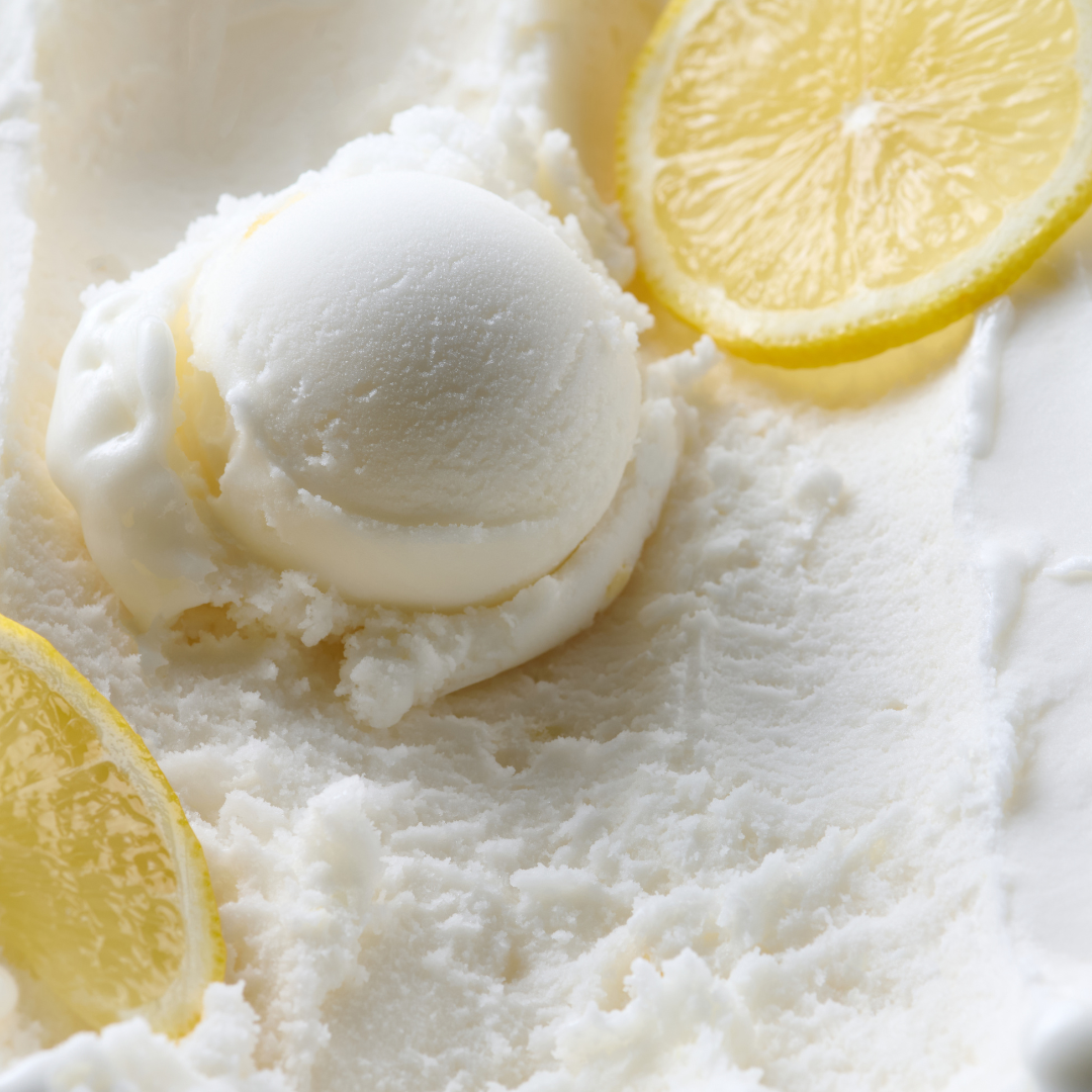 Eine Kugel Zitronensorbet auf cremiger Oberfläche mit Zitronenscheiben.
