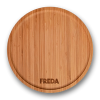 Runde Holzschneidebrett mit der Gravur "FREDA" am Rand, auf schwarzem Hintergrund.