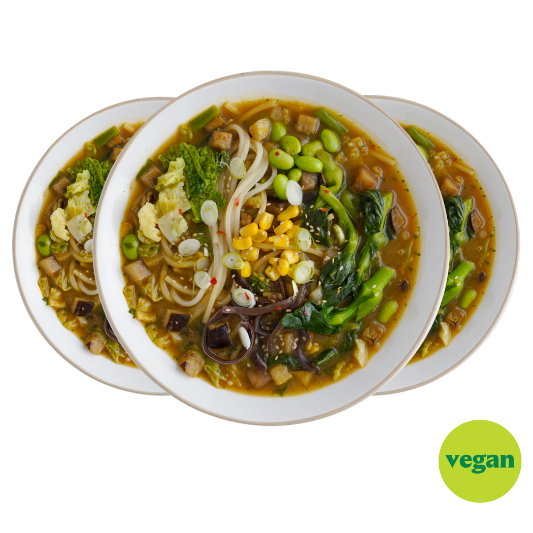 Drei Teller mit veganer Nudelsuppe, garniert mit Gemüse, Mais und Frühlingszwiebeln, auf weißem Hintergrund.