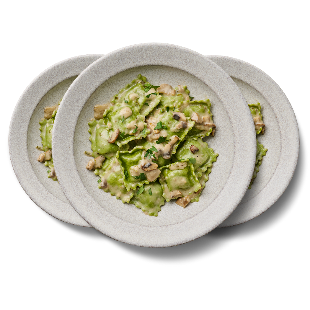 Drei Teller mit grünem Ravioli und Pilzen in cremiger Soße auf schwarzem Hintergrund.