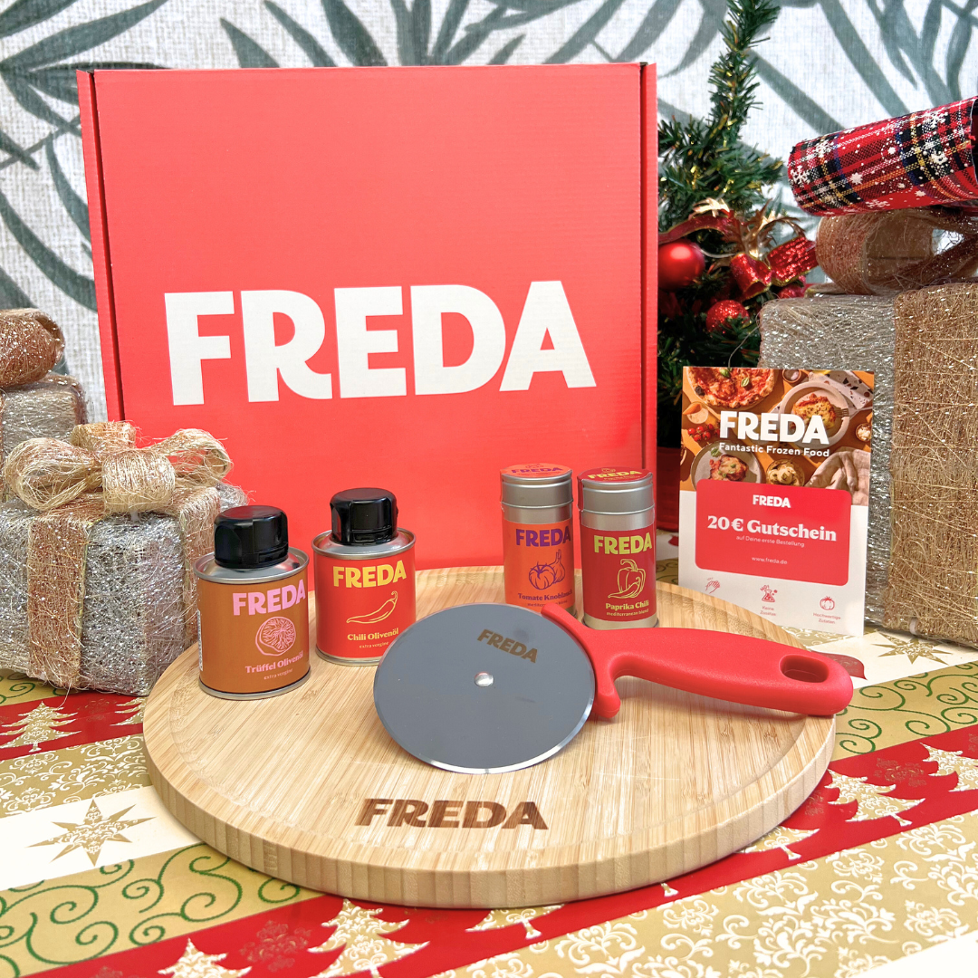 Geschenkset mit Freda-Produkten auf einem Schneidebrett, umgeben von Weihnachtsgeschenken und Dekoration.