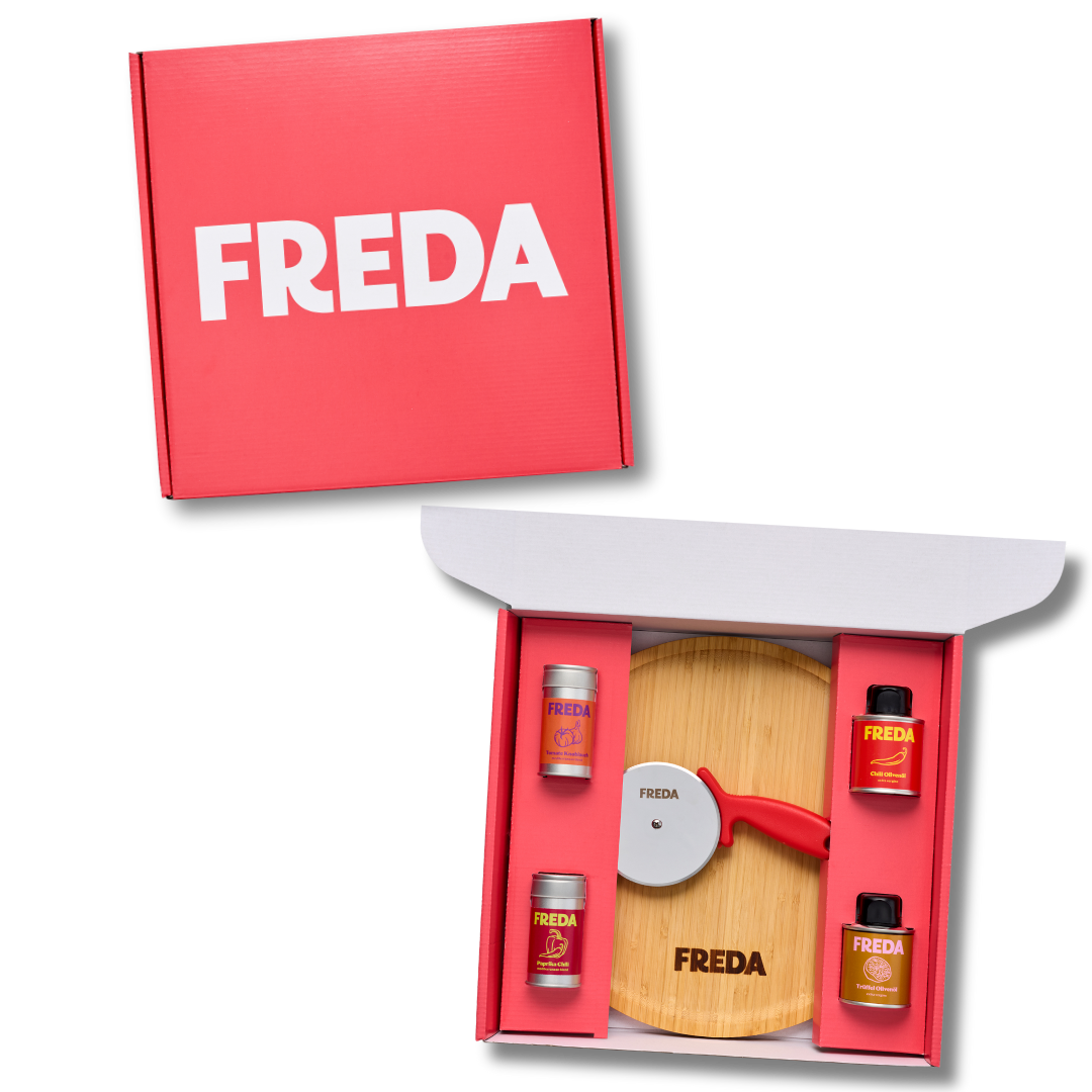 Rote Geschenkbox mit "FREDA"-Aufschrift, offen mit Kreisel, Holzkreis und vier Gewürzdosen im Inneren.