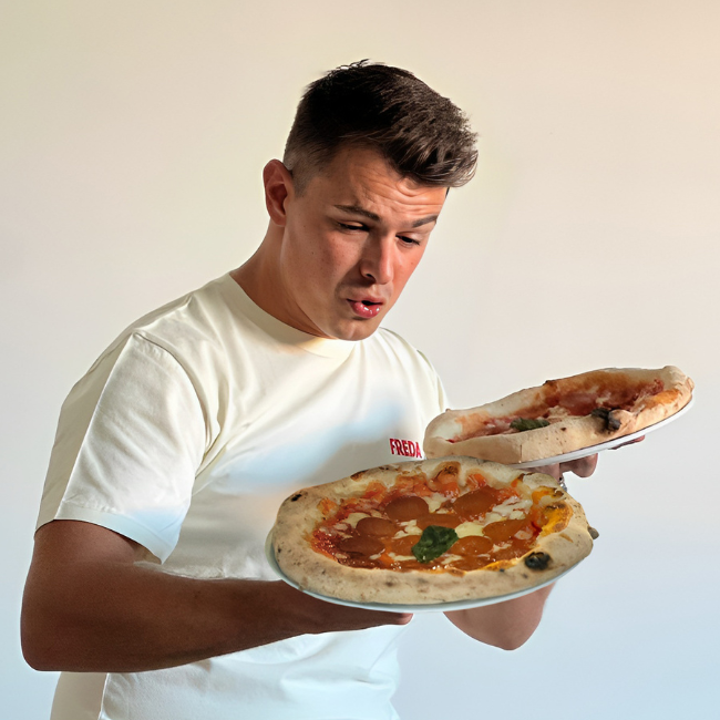Ein Mann im weißen T-Shirt hält zwei Pizzen und schaut überrascht auf sie.