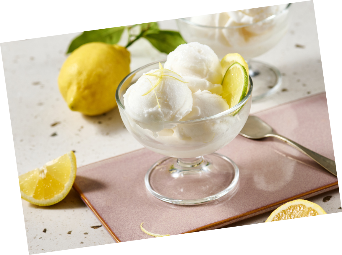 Eine Glasschale mit Zitronensorbet, garniert mit Zitronen- und Limettenscheiben, steht auf einem rosa Tablett.