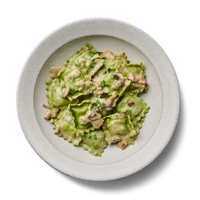 Grünes Ravioli-Gericht mit Pilzsahnesauce und Kräutern auf einem weißen Teller, vor schwarzem Hintergrund.