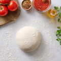 Teigkugel auf bemehlter Fläche, umgeben von Tomaten, Kräutern, Tomatensauce und Öl.