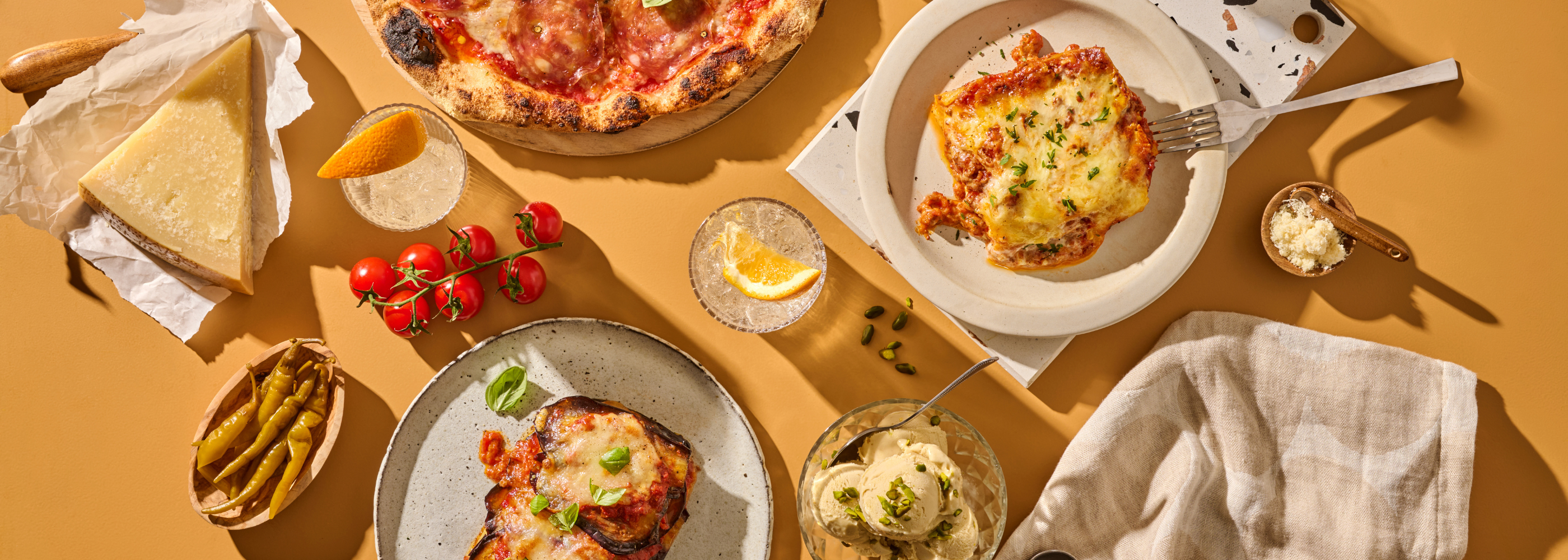 Eine Auswahl italienischer Speisen und Zutaten auf einem Tisch, darunter Pizza, Lasagne, Parmesan und Tomaten.