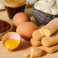 Zutaten für ein Dessert: Löffelbiskuits, zwei Eier, Kakaopulver, eine Schüssel Sahne und ein Glas Espresso.