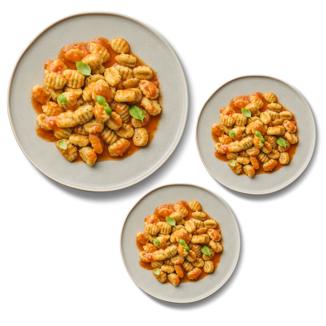 Drei Teller mit Gnocchi in Tomatensoße, garniert mit Basilikumblättern.