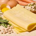 Frische Lasagneblätter mit Kichererbsen, Rosmarin, Karotten und einem aufgeschlagenen Ei auf einem Tisch.