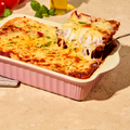 Eine frisch gebackene Lasagne in einer rosa Auflaufform mit einem servierten Stück auf einer Gabel.