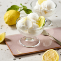 Zwei Schalen Zitronensorbet auf einem Tisch mit frischen Zitronen und einem Löffel daneben.
