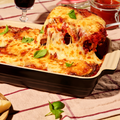 Überbackene Lasagne in einer Auflaufform mit Käse und Basilikumblättern, Portion wird serviert.